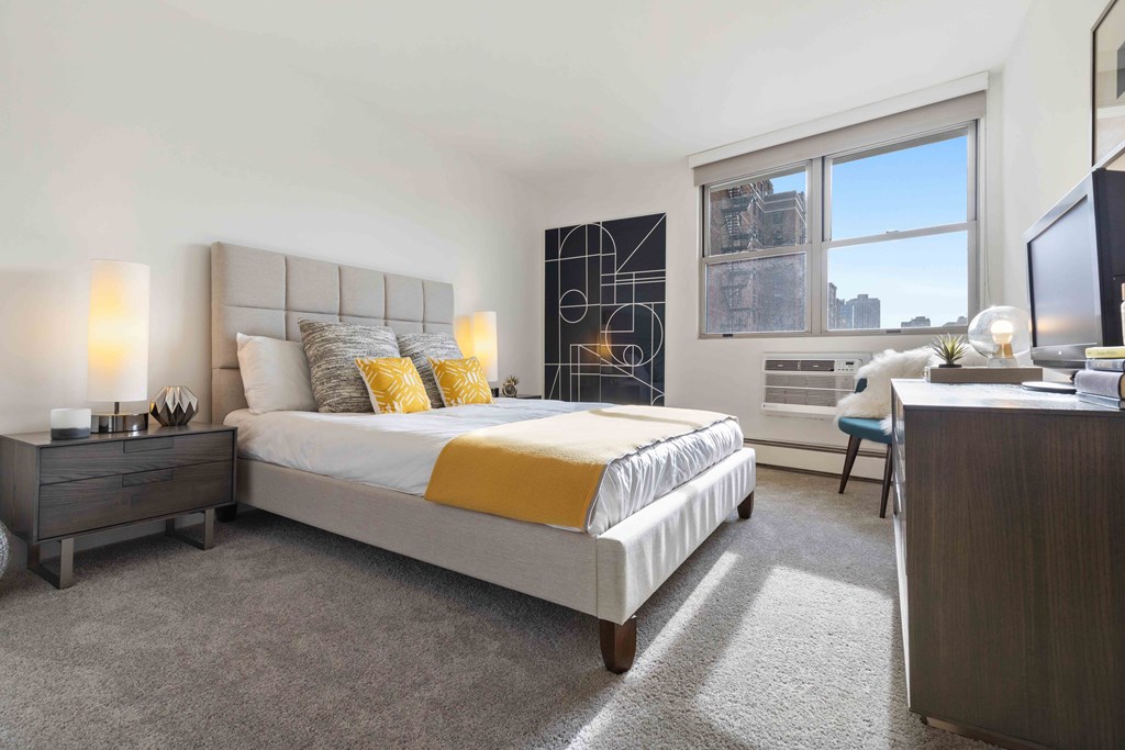 Apartments For Rent In Chicago Lakeview - Bedroom With Bed, Modern Decor, Nightstands, Chair, Dresser, Window, And AC.