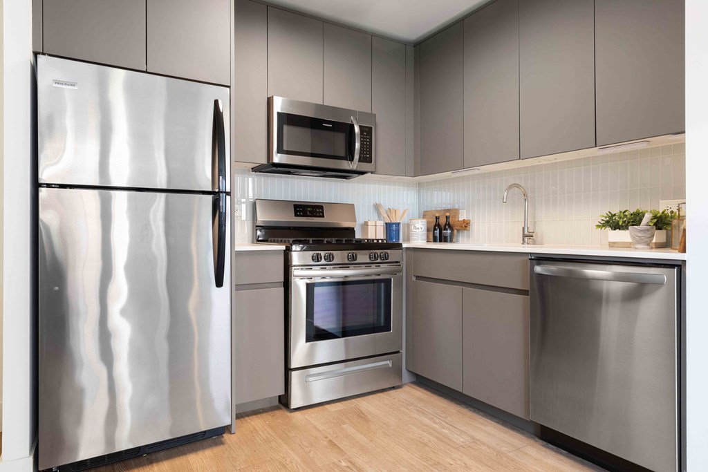 Apartments for Rent Chicago Lakeview IL - Wave Lakeview - Modern Open Concept Kitchen With Energy Star Rated Stainless Steel Appliances, Wood-Look Plank Flooring, Lacquered Matte Grey Cabinetry, Tile Backsplash, Full Sized Dishwasher, And Built-In Microwave