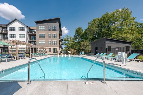 North Indianapolis, IN, Apartments Near Monon Trail - North End Apartments - Resort-Style Swimming Pool With Sundeck Lounge Chairs, Pergola, Metal Fence, and Community Buildings.