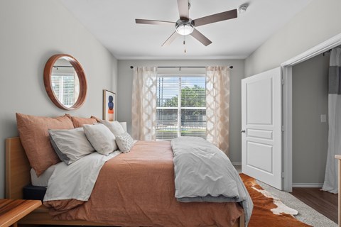 A bedroom with a bed, a ceiling fan, and a window with curtains.