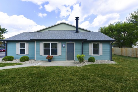 2-Bedroom Apartments in St. Vincent Greenbriar, Indianapolis, IN - The Jameson - Outdoor View of a Single-Story House with Blue Siding, Door, Windows, Plants, and Lawn.