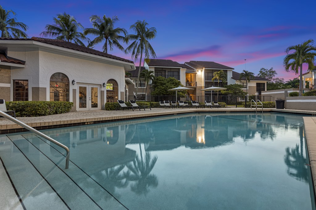 a large swimming pool with lounge chairs and umbrellas in front of a building