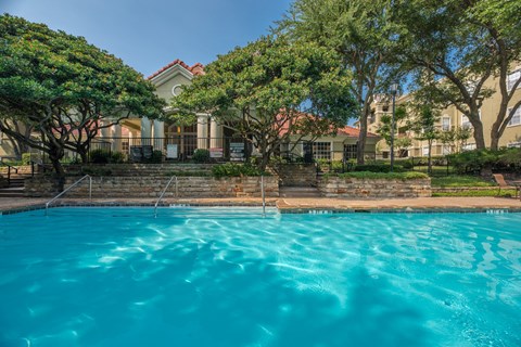 A swimming pool in front of a house with trees.