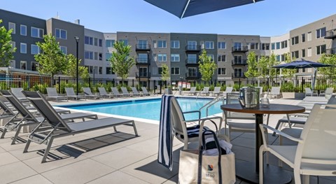 A pool area with chairs and umbrellas in front of apartment buildings.