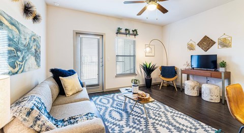A living room with a beige couch, a blue and white patterned rug, a wooden chair, and a television on a wooden stand.
