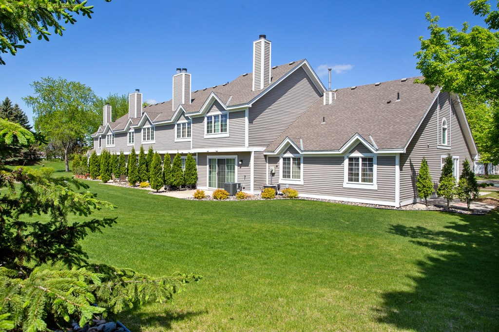 Townhomes For Rent In Woodbury - Rear Exterior View Of Townhome, Lush Green Grass, Shrubs, And Trees Surround The Area.