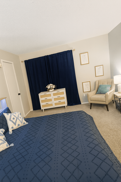 A bedroom with a bed, chair, and nightstand.