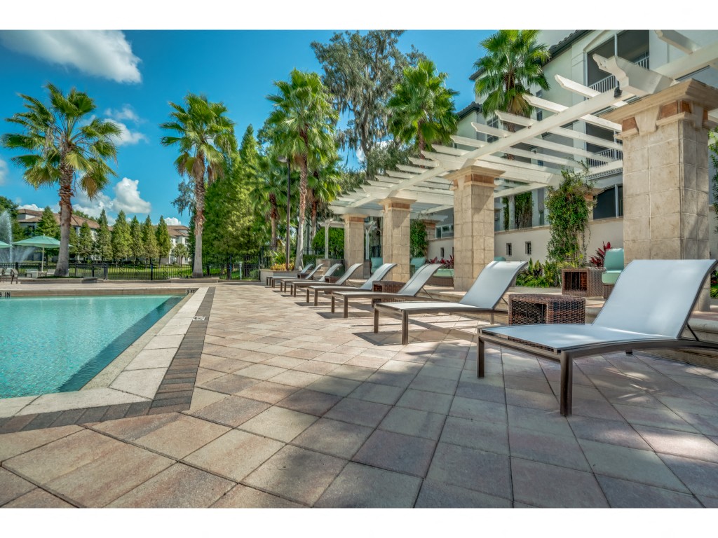 a pool and lounge chairs in front of a building with palm trees