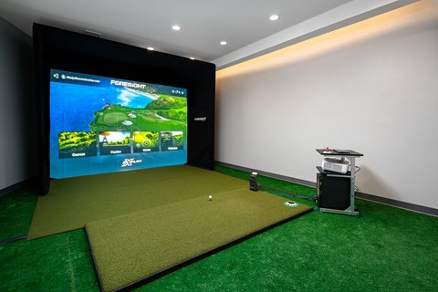 A golf simulator room with a screen showing a golf course and a ball on the ground.