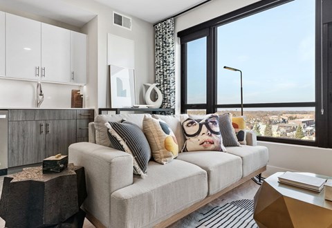 A modern living room with a grey couch and a large window overlooking a cityscape.