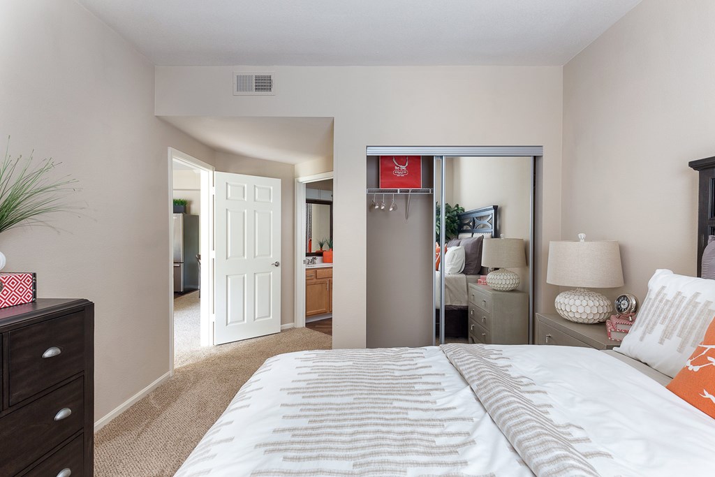 1, 2, & 3-BR Apartments in Overland Park, KS - The Highlands - Bedroom With Carpeting, Full-Size Bed, Dresser, Mirror Closet Door, And Bathroom Entrance