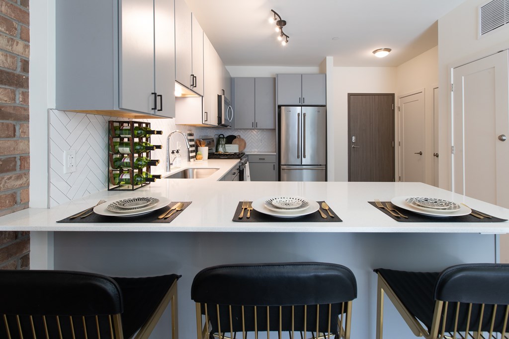 Maple Street Lofts - Kitchen With Light Grey Cabinets, Appliances, Track Lighting, and Breakfast Bar.