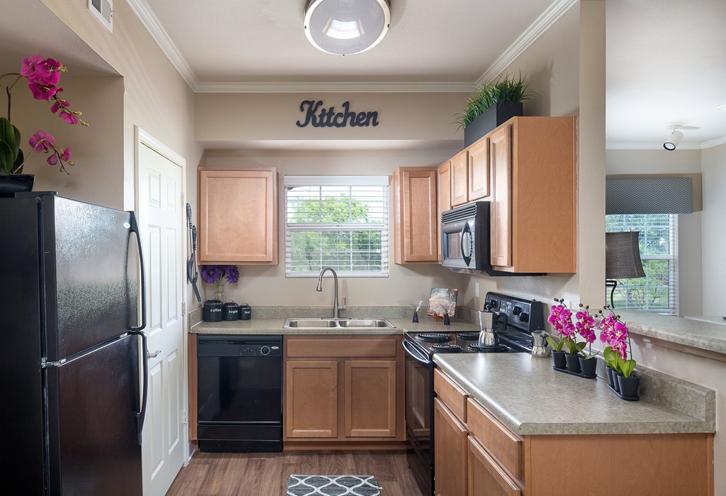 Overland Park Apartments - The Highlands - Kitchen With Black Appliances, Wooden Cabinets, Wood-Style Flooring, And Spacious Granite Countertops