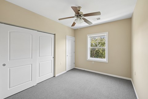 A room with a ceiling fan and a window showing trees outside.