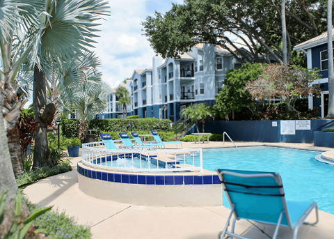 A pool surrounded by trees and chairs.