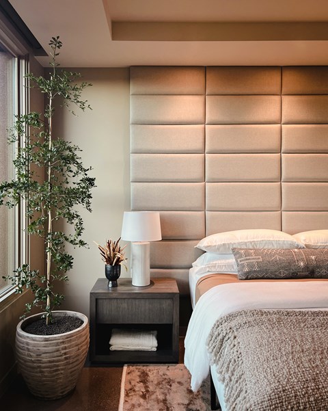 A bedroom with a bed, nightstand, and a potted plant.