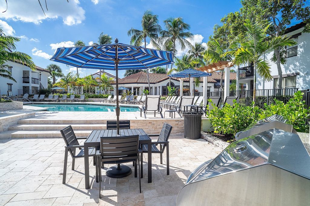 Grilling station with table, umbrella, and chairs next to pool deck
