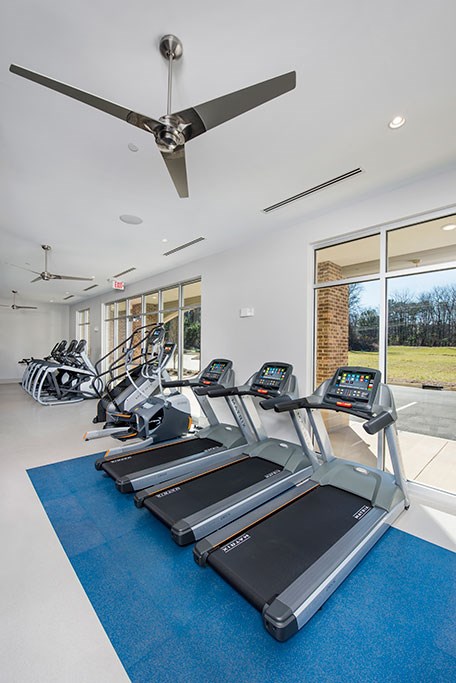 a gym with cardio machines and a ceiling fan