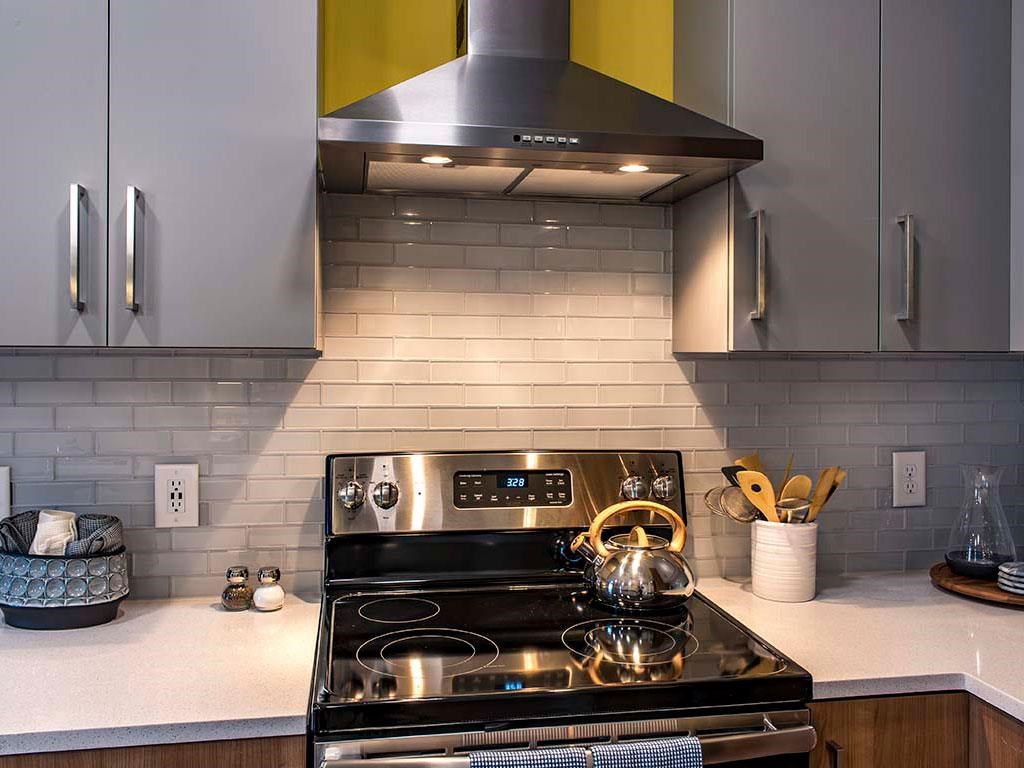 View of stainless steel stove with hood, gray cabinets and tile backsplash