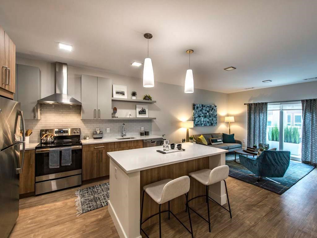 Model apartment kitchen with stainless steel appliances, island and living room in background
