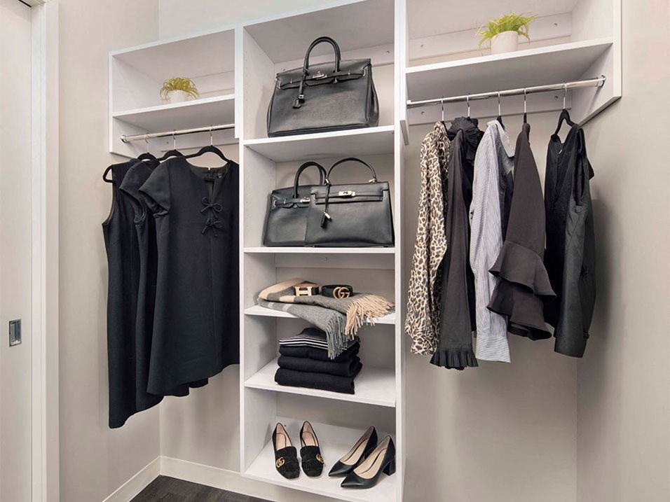 a walk in closet with a white shelving unit filled with clothes and bags