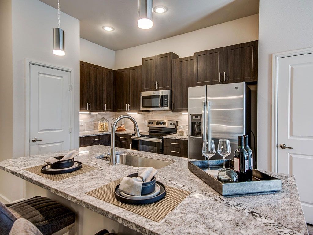 Granite counter tops, stainless appliance package, medium brown cabinets, plank wood-style flooring, island seating, abundant cabinet and pantry space