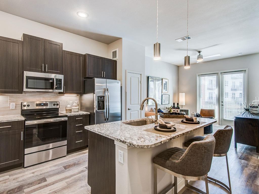 Granite counter tops, stainless appliance package, medium brown cabinets, plank wood-style flooring, island seating, abundant cabinet and pantry space