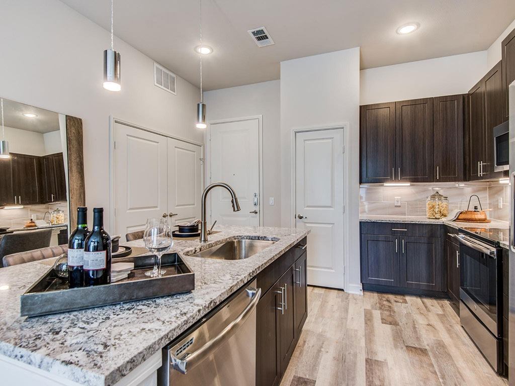 Granite counter tops, stainless appliance package, medium brown cabinets, plank wood-style flooring, island seating, abundant cabinet and pantry space