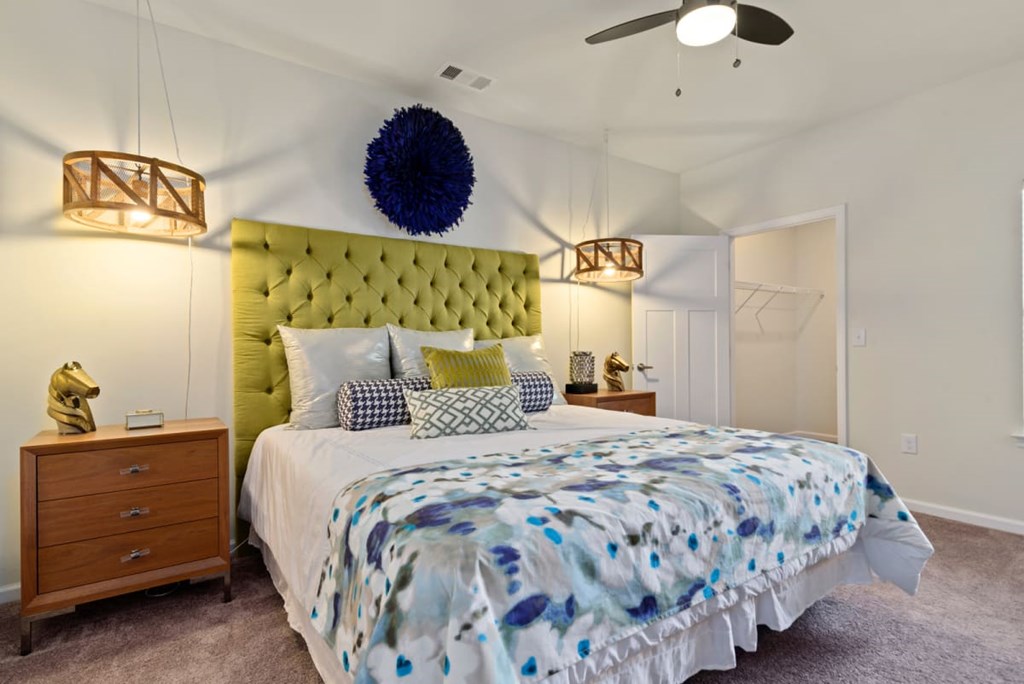 inside-bedroom-ashland-farms-ashland-city-tn One-Bedroom Apartments in Ashland City, TN - Ashland Farms - Bedroom with Carpeted Flooring, Large Bed, Wooden Nightstands with Drawers, Hanging Lamps, Spacious Closet, and Ceiling Fan.