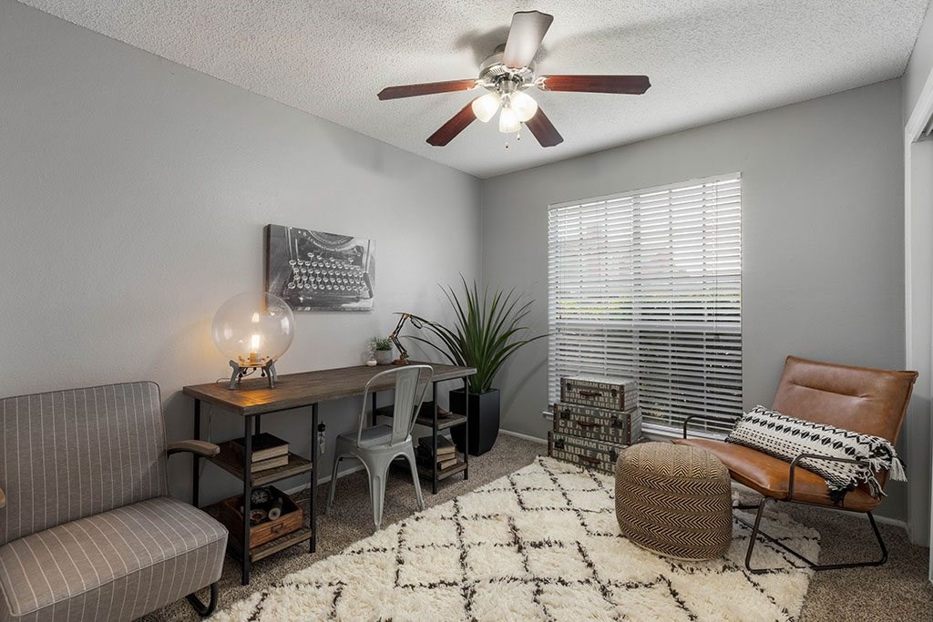 a living room with a desk and a ceiling fan