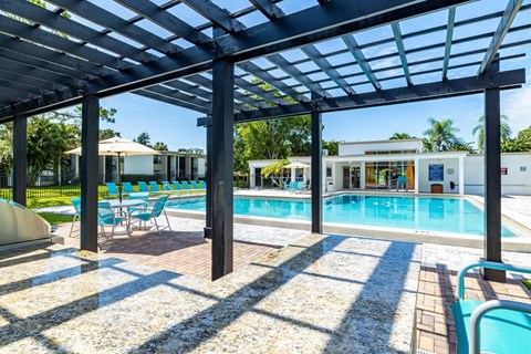 A pool area with a wooden pergola and blue chairs.