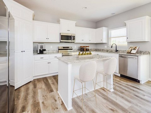 A kitchen with white cabinets and a marble island.