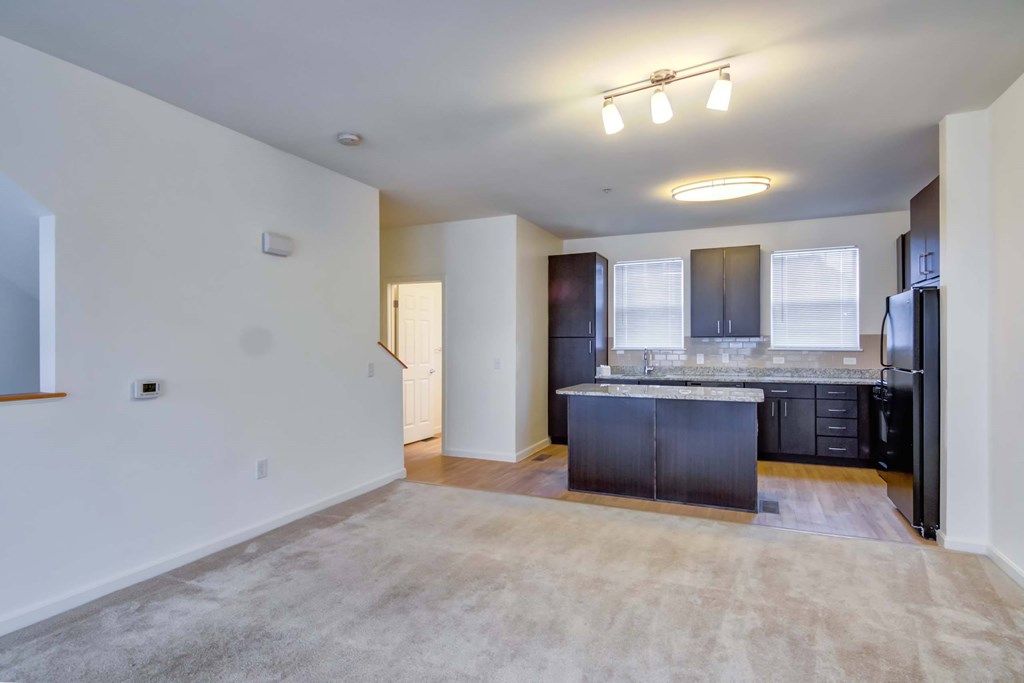 an empty living room with a kitchen with black appliances