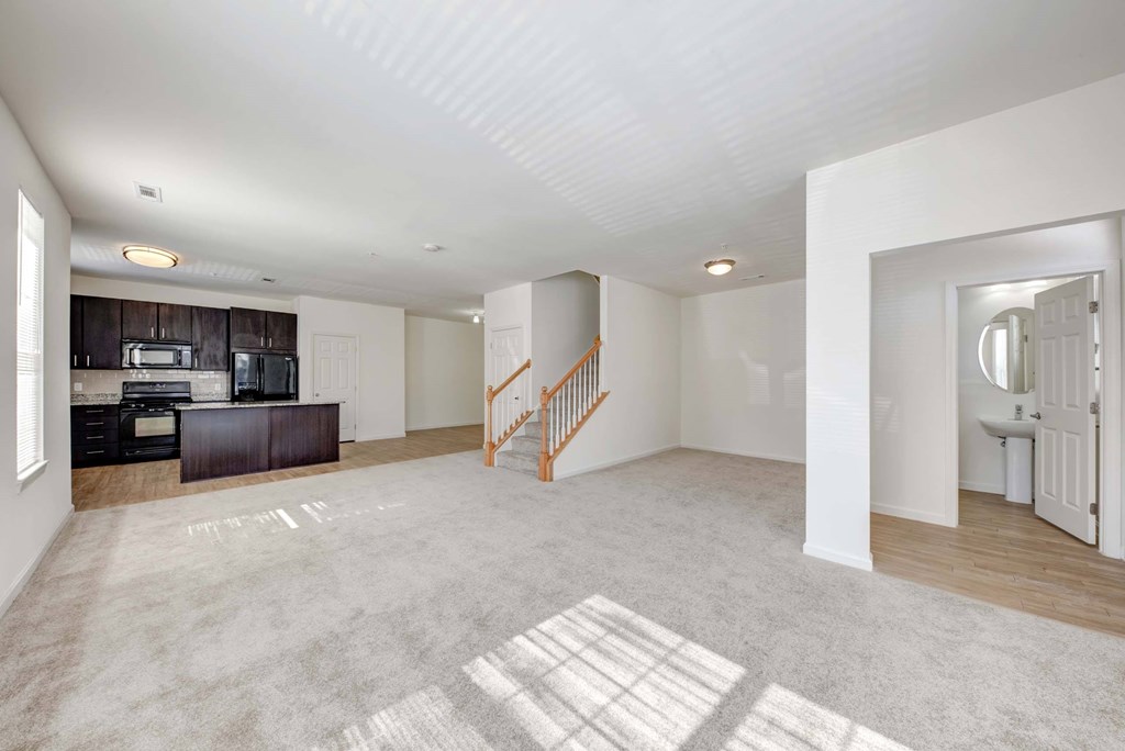 an empty living room with a kitchen and a staircase