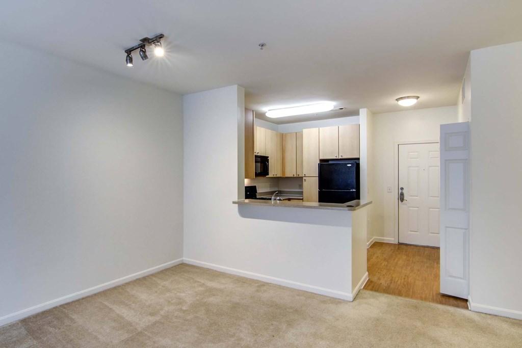 an empty living room with a kitchen and a ceiling fan