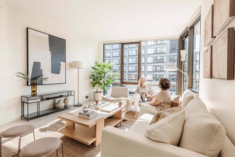 two people sitting on a couch in a living room with a large window