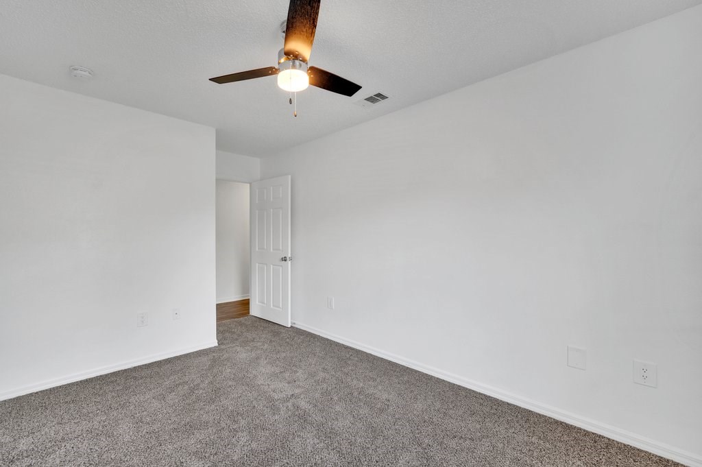 the spacious living room with white walls and a ceiling fan