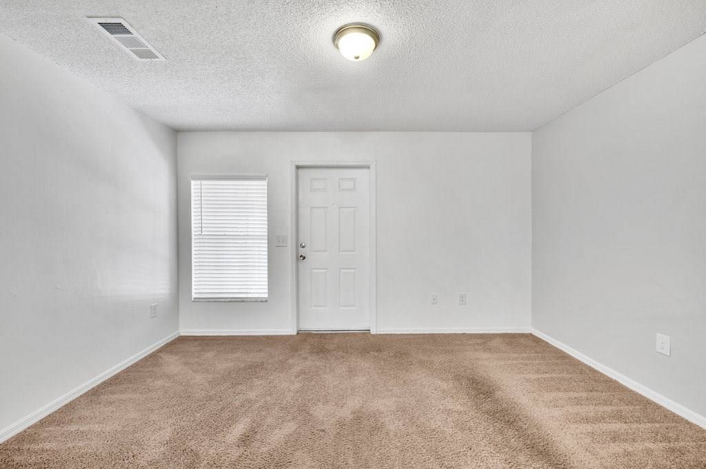 an empty living room with a white door and carpet