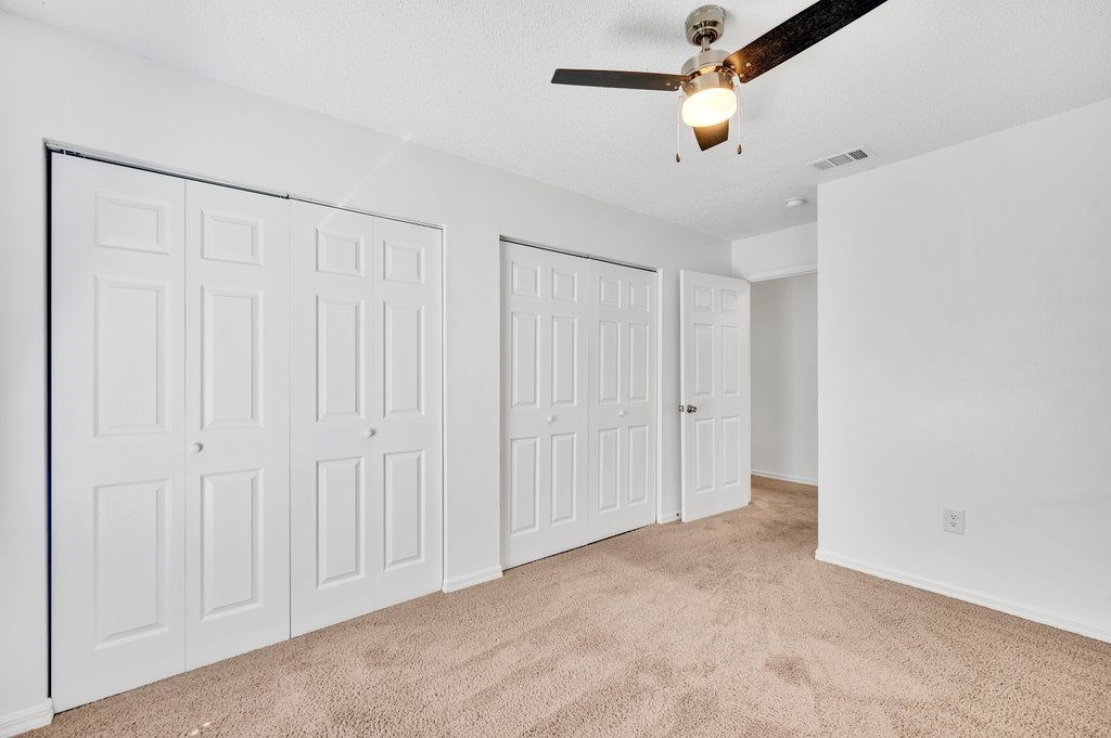 an empty bedroom with a ceiling fan and white closets