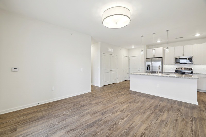 the living room and kitchen of an apartment with white walls and wood flooring