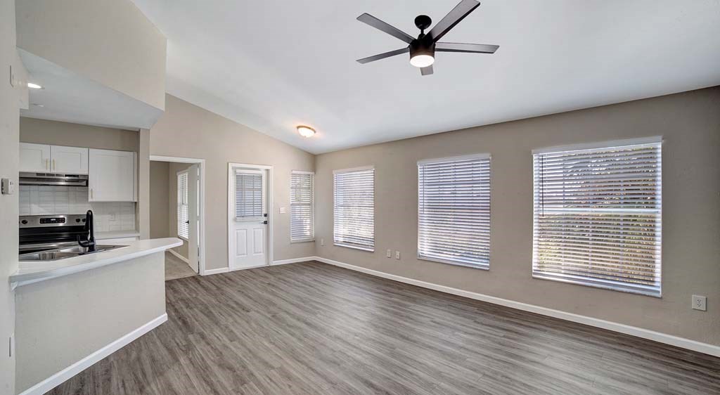 an empty living room with a ceiling fan and a kitchen