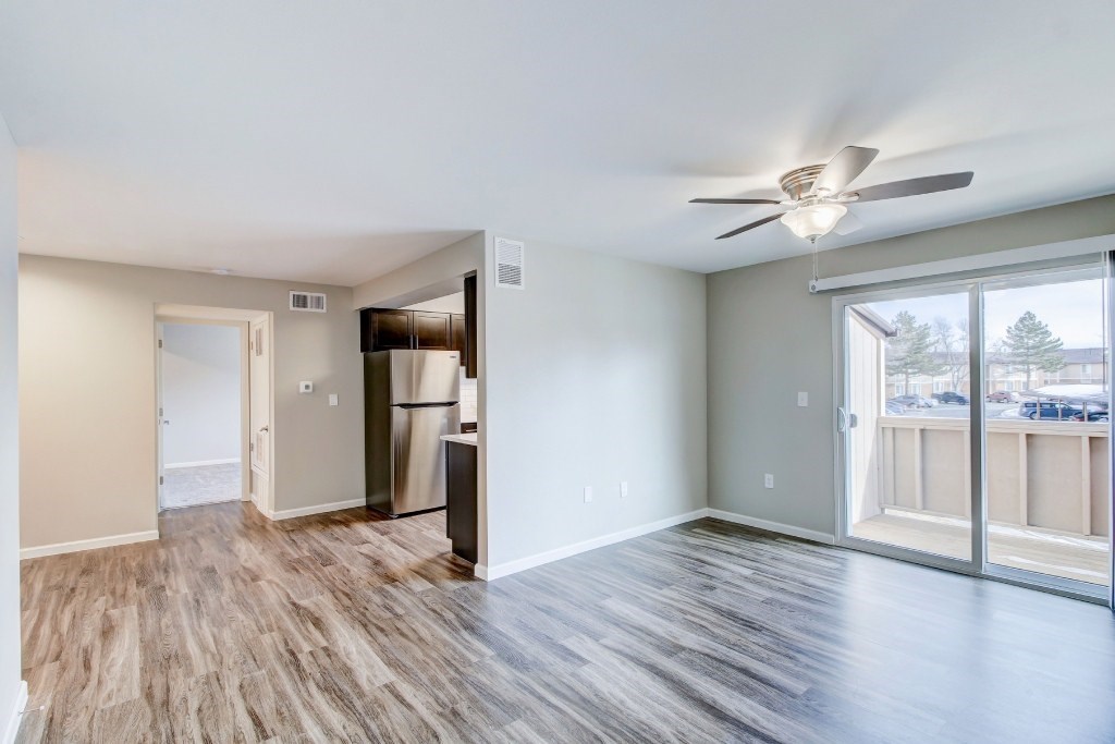 an empty living room with a large window and a ceiling fan