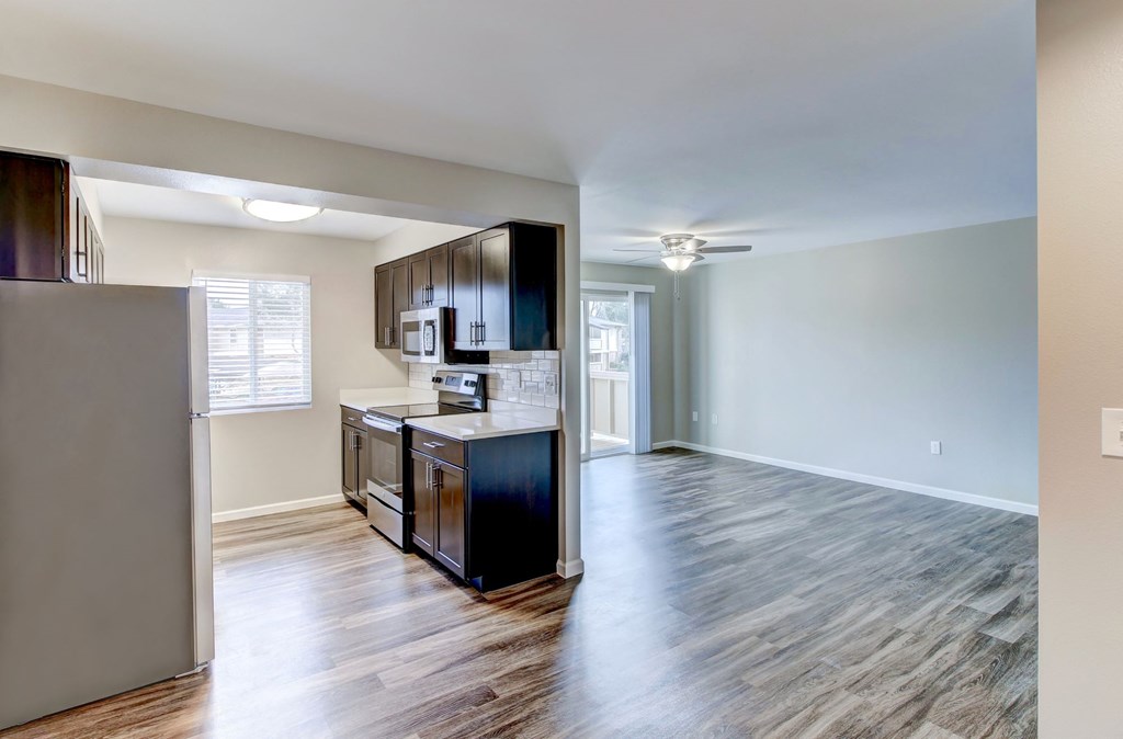 an empty living room with a kitchen with a refrigerator and a microwave