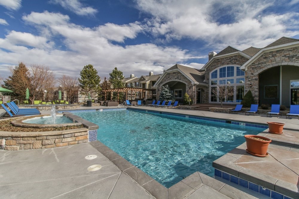 a swimming pool with blue chairs and a house in the background