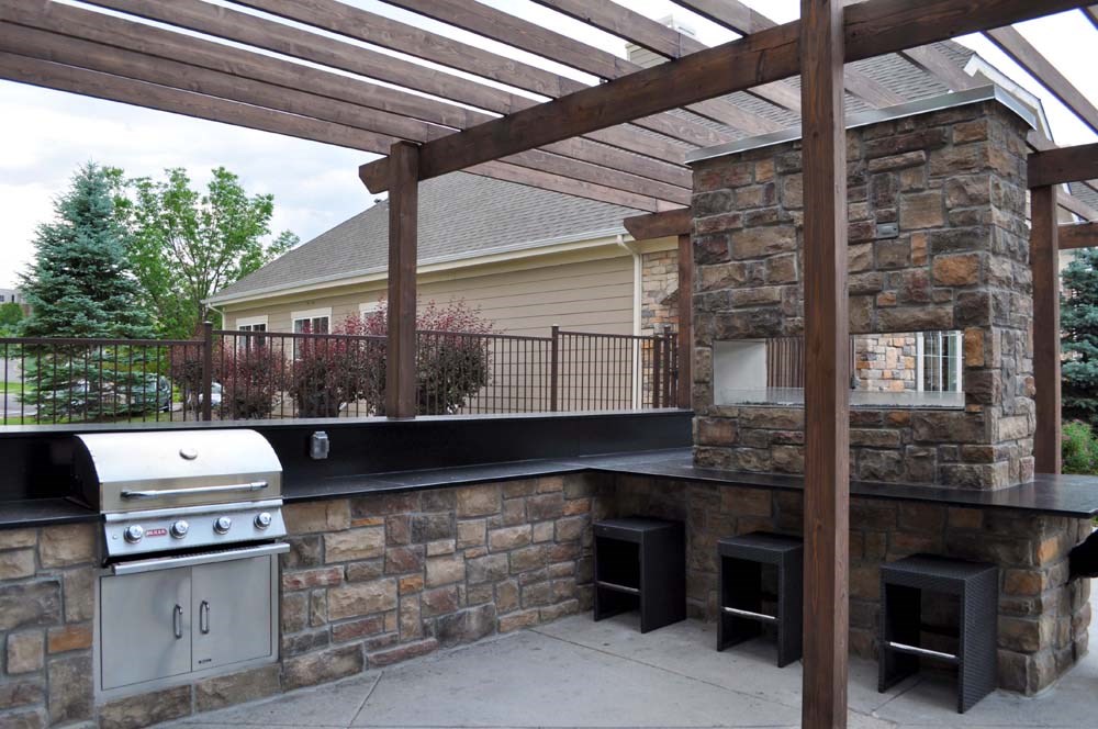 a outdoor kitchen with a stone wall and a pergola