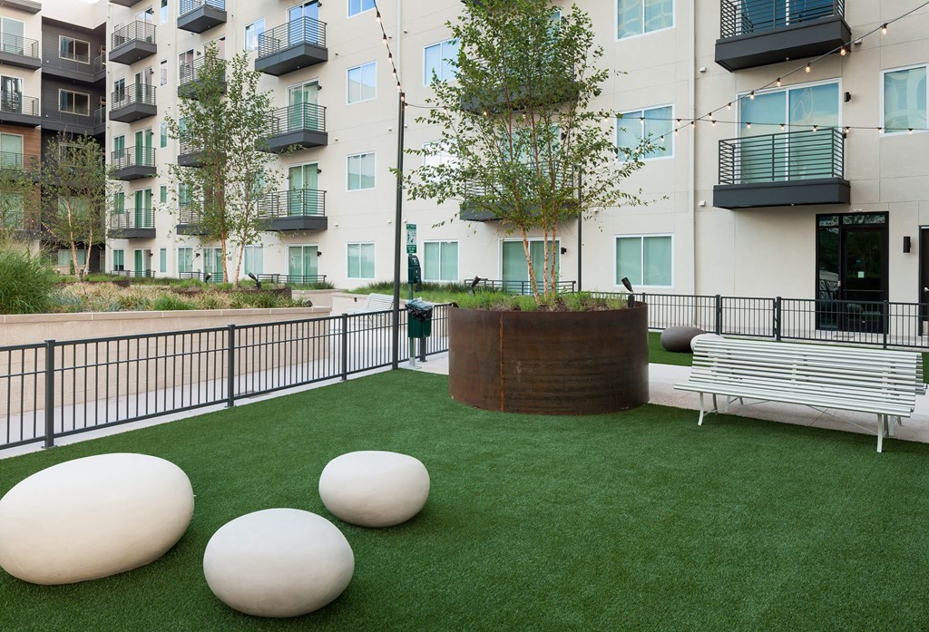 a courtyard with grass and benches and a tree in front of an apartment building