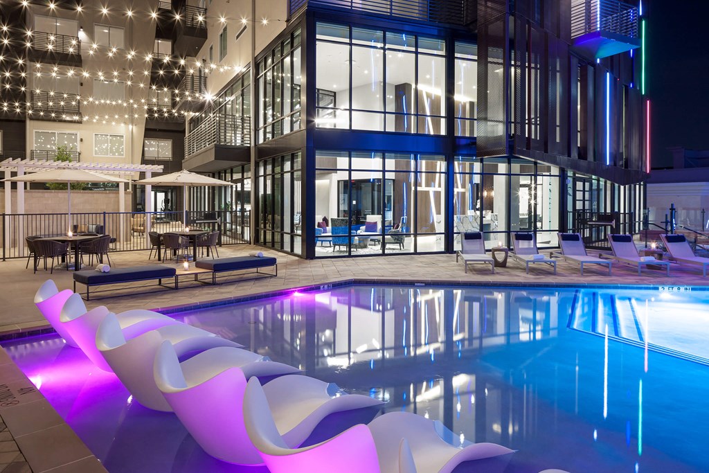 a swimming pool at night with lounge chairs next to it