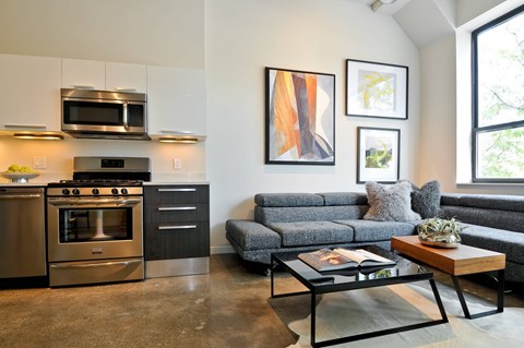 A modern kitchen with a stainless steel oven and microwave, a grey sofa, and a coffee table with a book on it.