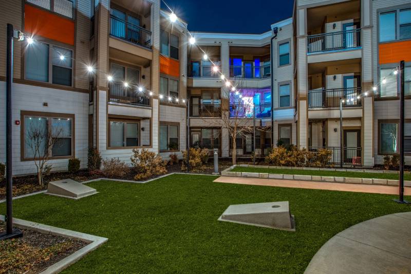 an apartment yard with grass and lights at night