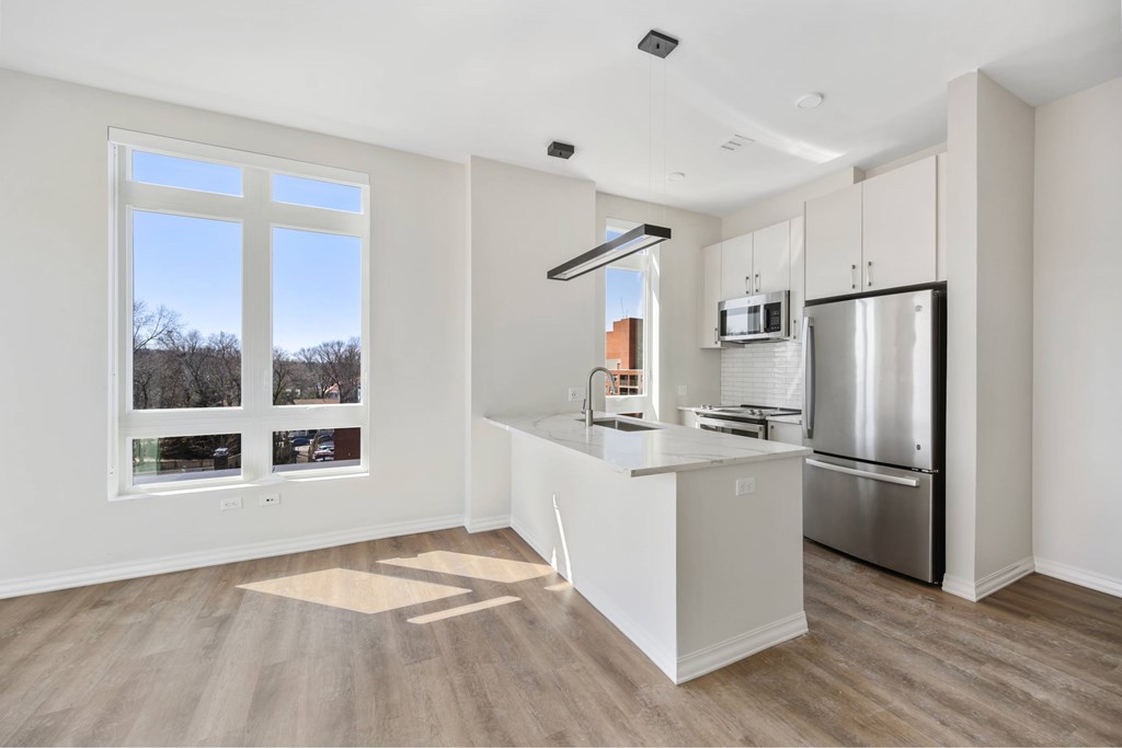 a white kitchen with a large window and a stainless steel refrigerator